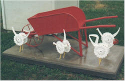 photo of red wheelbarrow surrounded by white chickens made of bicycle gears